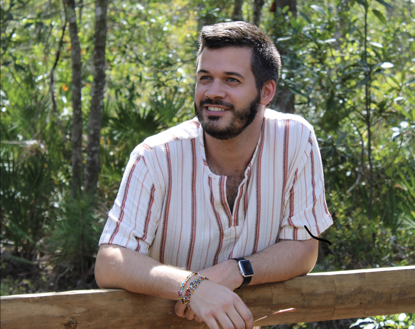 Me standing next to a wooden fence in the woods of a nature trail.